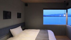 A bedroom with a bed, a window with a view of water and mountains, and a ceiling with wooden beams. - Torch Amano-hashidate (Yonezawa)
