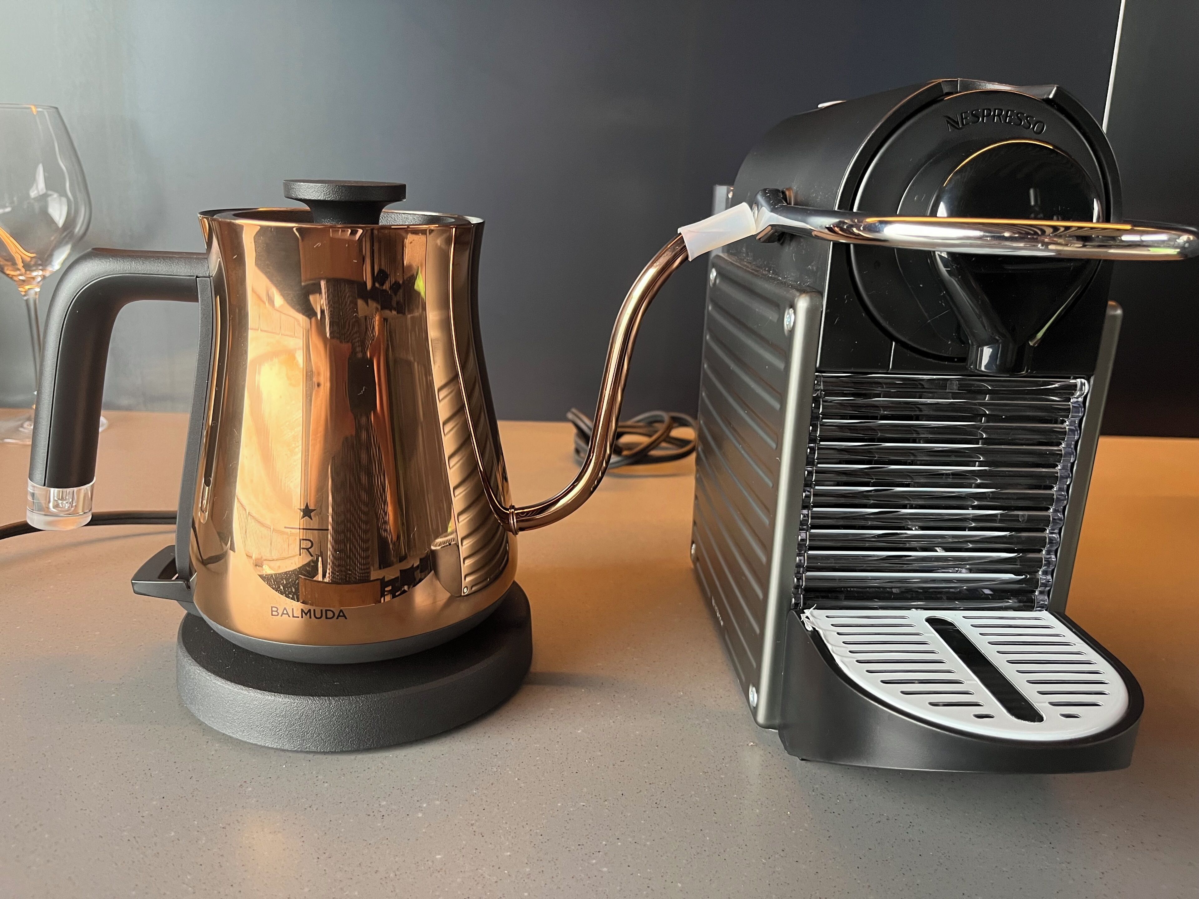 A coffee machine with a transparent water tank and a black base, connected to a black coffee maker with a drip tray.