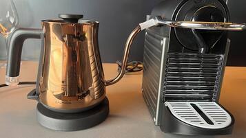 A coffee machine with a transparent water tank and a black base, connected to a black coffee maker with a drip tray.