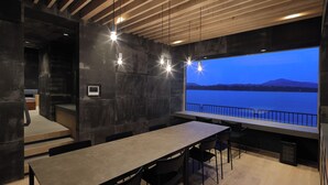 A modern interior with a long table, chairs, and a large window overlooking a body of water. - Torch Amano-hashidate (Yonezawa)