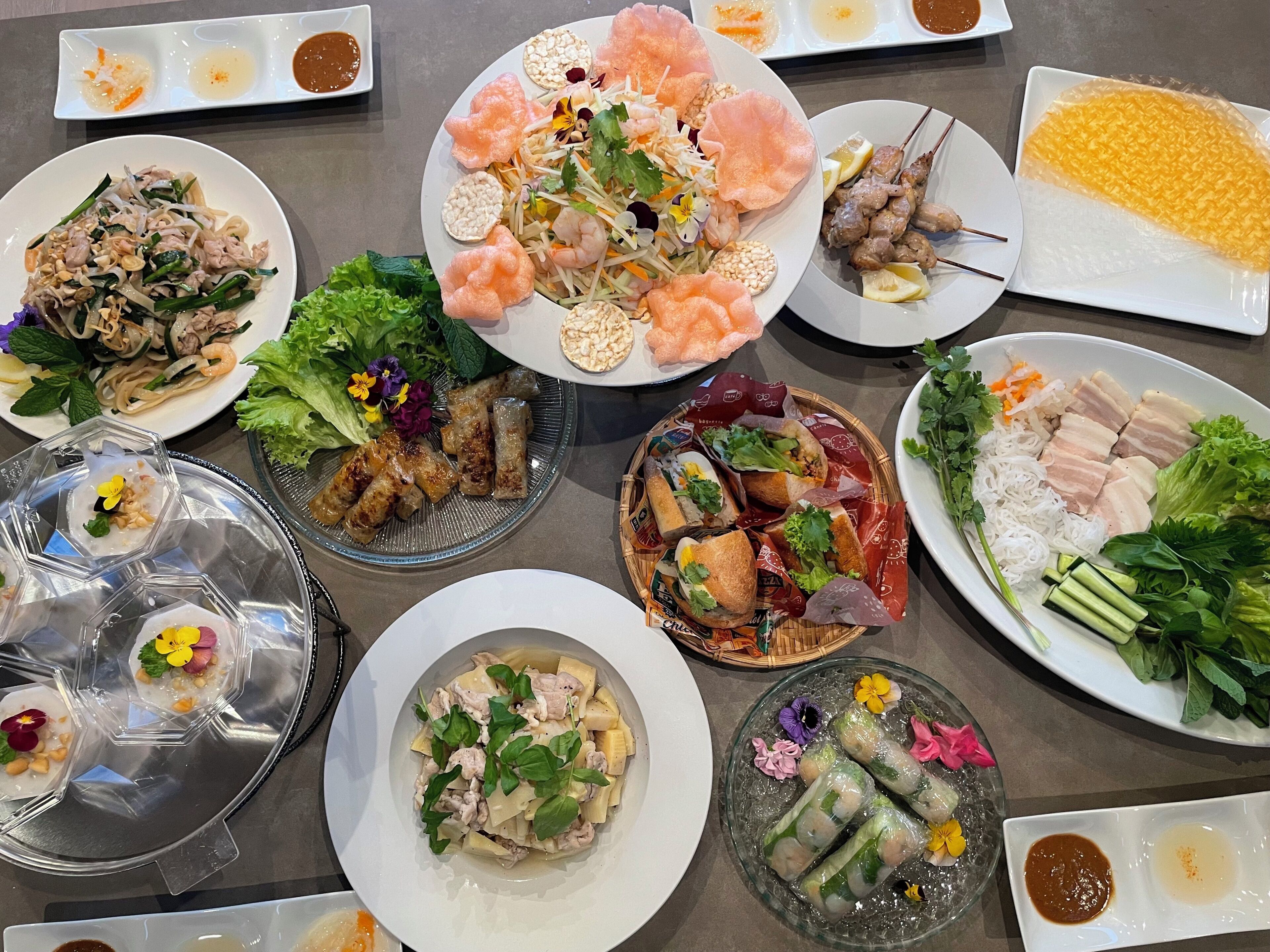 A variety of dishes including spring rolls, noodles, and grilled meats, suggesting a diverse meal selection.