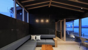 A modern interior with a grey sectional sofa, a wooden coffee table, and a view of a balcony with a table and chairs. - Torch Amano-hashidate (Yonezawa)