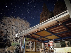 Un espacio al aire libre cubierto con un telescopio, una silla y una mesa bajo un cielo nocturno estrellado.