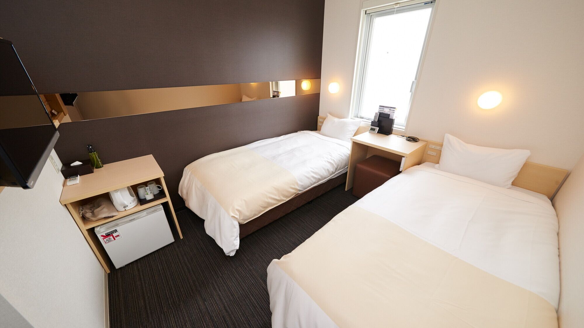 A hotel room with two beds, a desk, a small refrigerator, and a TV.