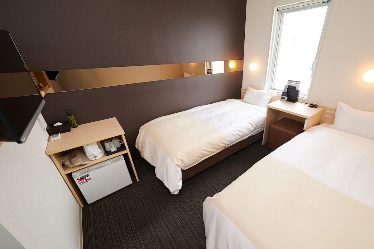 Ein Hotelzimmer mit zwei Betten, einem Schreibtisch, einem kleinen Kühlschrank und einem Fernseher.