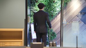 A man in a suit walking through a glass door with a green wall and a wooden floor. - Super Hotel JR Nara Station Sanjo Street (Hikone)