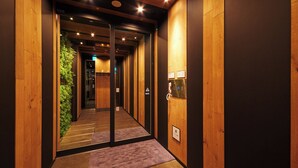 A hallway with wooden walls, a glass elevator door, and a green wall with plants. - Super Hotel JR Nara Station Sanjo Street (Hikone)