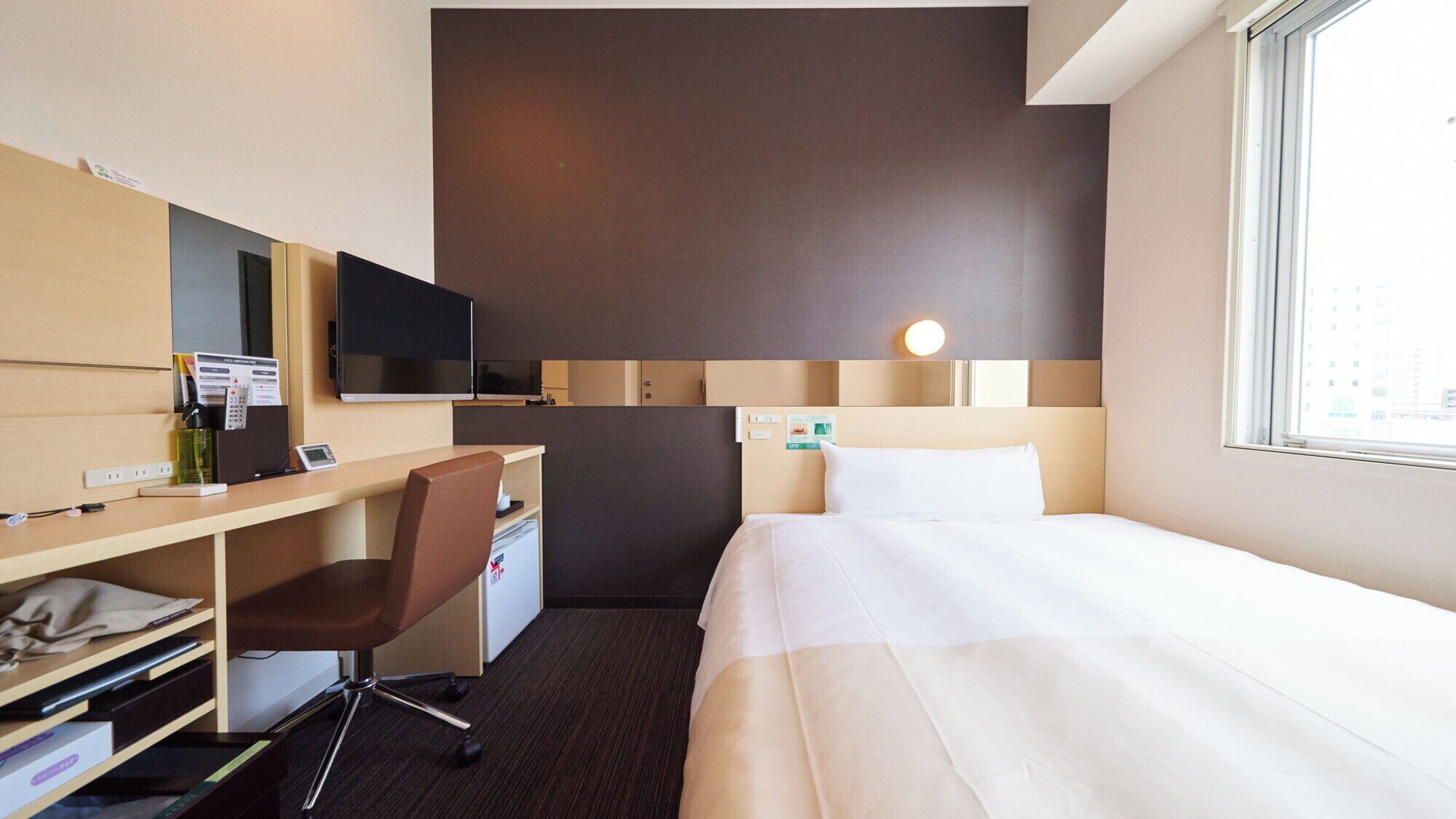 A hotel room with a bed, a desk with a chair, a television, and a window.