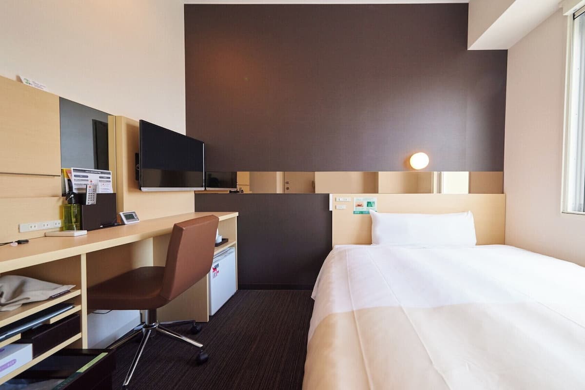 Ein Hotelzimmer mit einem Bett, einem Schreibtisch mit Stuhl, einem Fernseher und einem Fenster.
