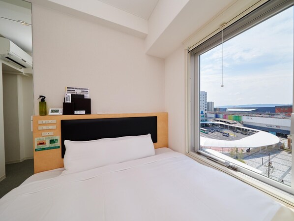A hotel room with a bed, a control panel, a window with a view of a cityscape. - Super Hotel JR Nara Station Sanjo Street (Hikone)