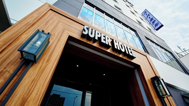 A hotel entrance with a sign reading 'SUPER HOTEL' and a large window reflecting the sky. - Super Hotel JR Nara Station Sanjo Street (Hikone)