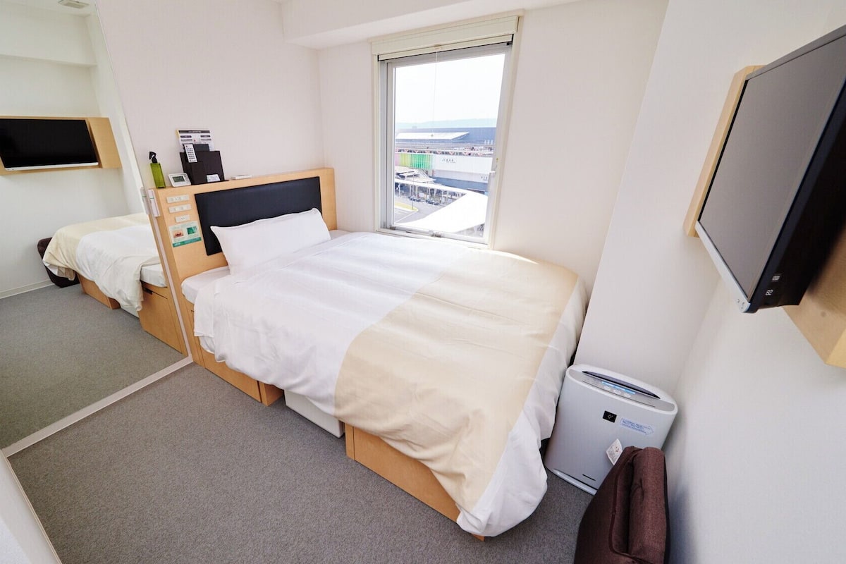 Ein Hotelzimmer mit zwei Betten, einem Fernseher, einem Fenster mit Blick und einer Heizung.