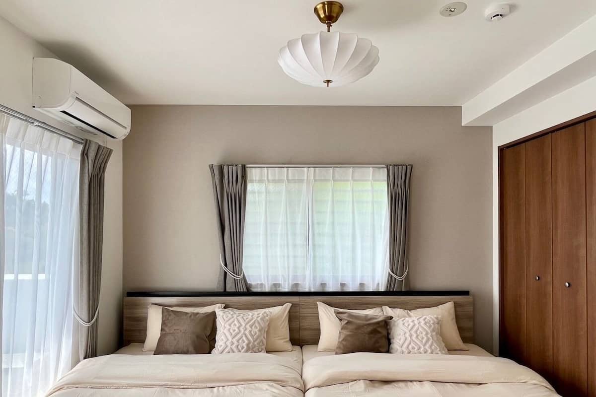 Un dormitorio con una cama grande, una ventana con cortinas, un equipo de aire acondicionado y una lámpara en el techo.