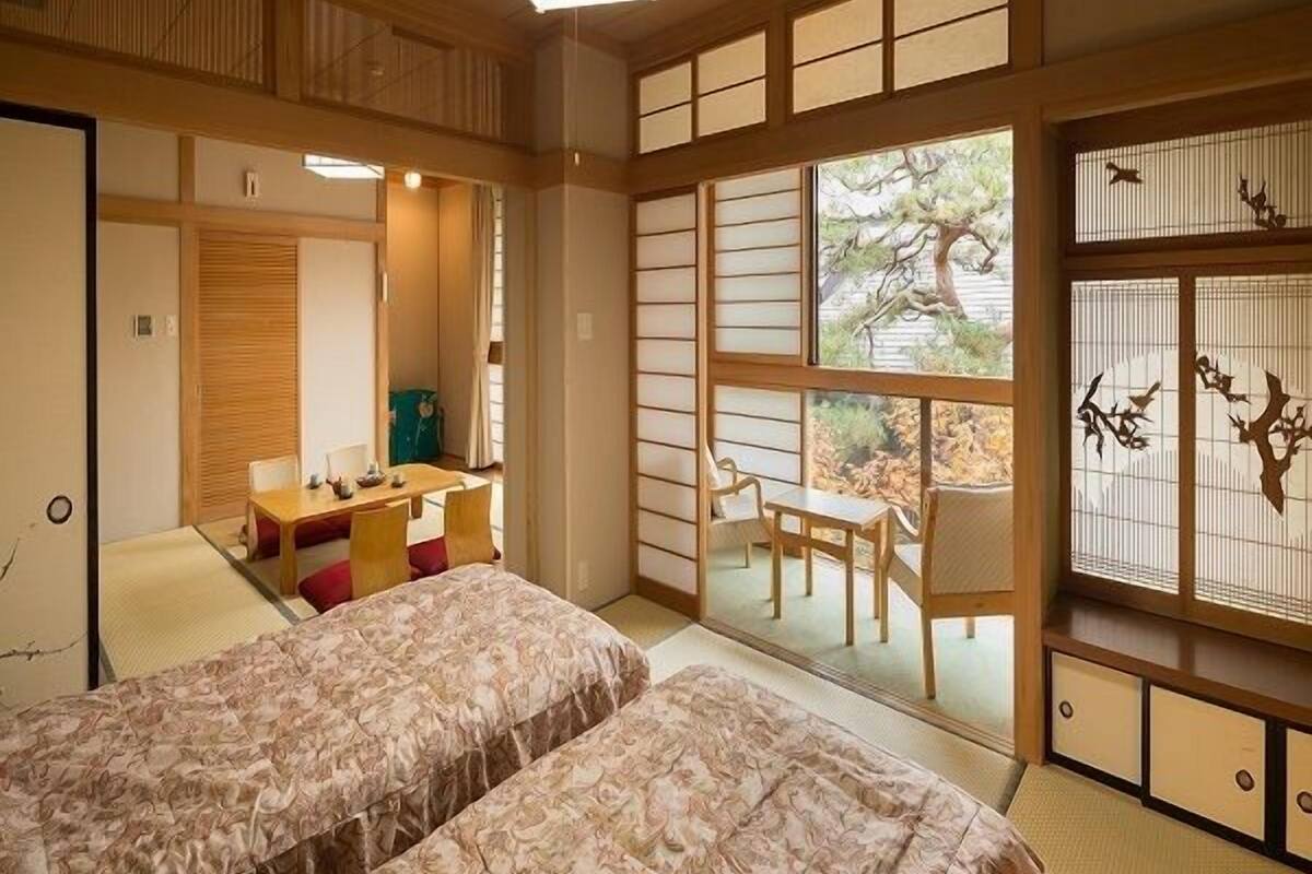 Ein traditioneller japanischer Raum mit Tatami-Boden, Futon-Bett, kleinem Schreibtisch und einer Schiebetür zu einem Außenbereich.