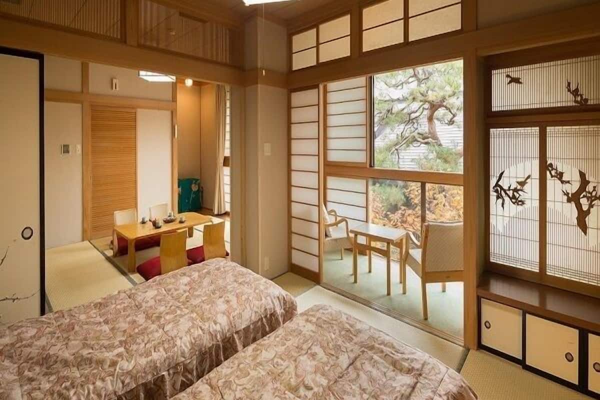 Um quarto em estilo tradicional japonês com piso de tatame, futon, uma pequena escrivaninha e uma porta deslizante que dá para uma área externa.