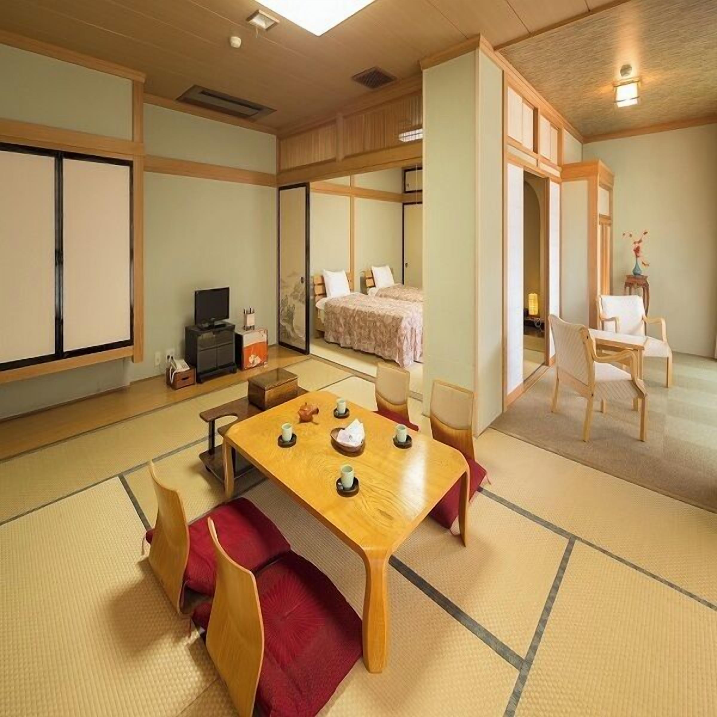 Um quarto em estilo japonês tradicional, com piso de tatame, uma mesa baixa com xícaras e uma cama com colcha rosa.