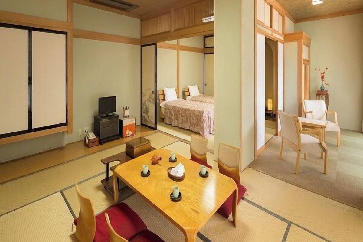 Ein traditioneller japanischer Raum mit Tatami-Bodenbelag, einem niedrigen Tisch mit Tassen und einem Bett mit einer rosa Tagesdecke.