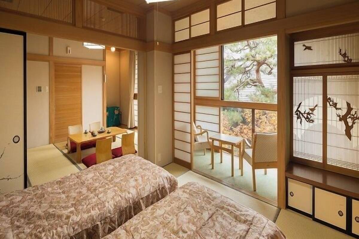 Ein traditioneller japanischer Raum mit Tatami-Bodenbelag, einem niedrigen Tisch mit Kissen und einer verschiebbaren Tür zu einem Außenbereich.