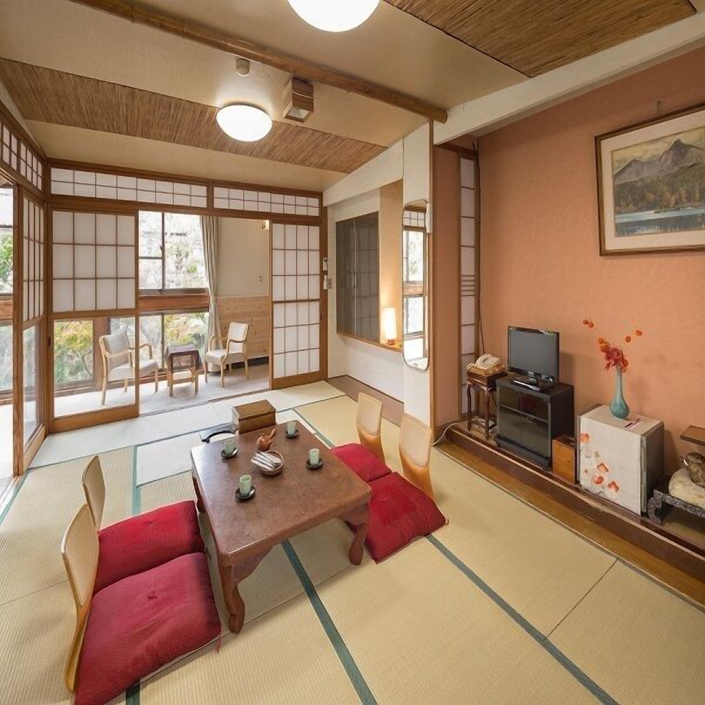 Um quarto em estilo japonês tradicional com tatames, uma mesa de madeira baixa com almofadas, uma televisão e um quadro na parede.
