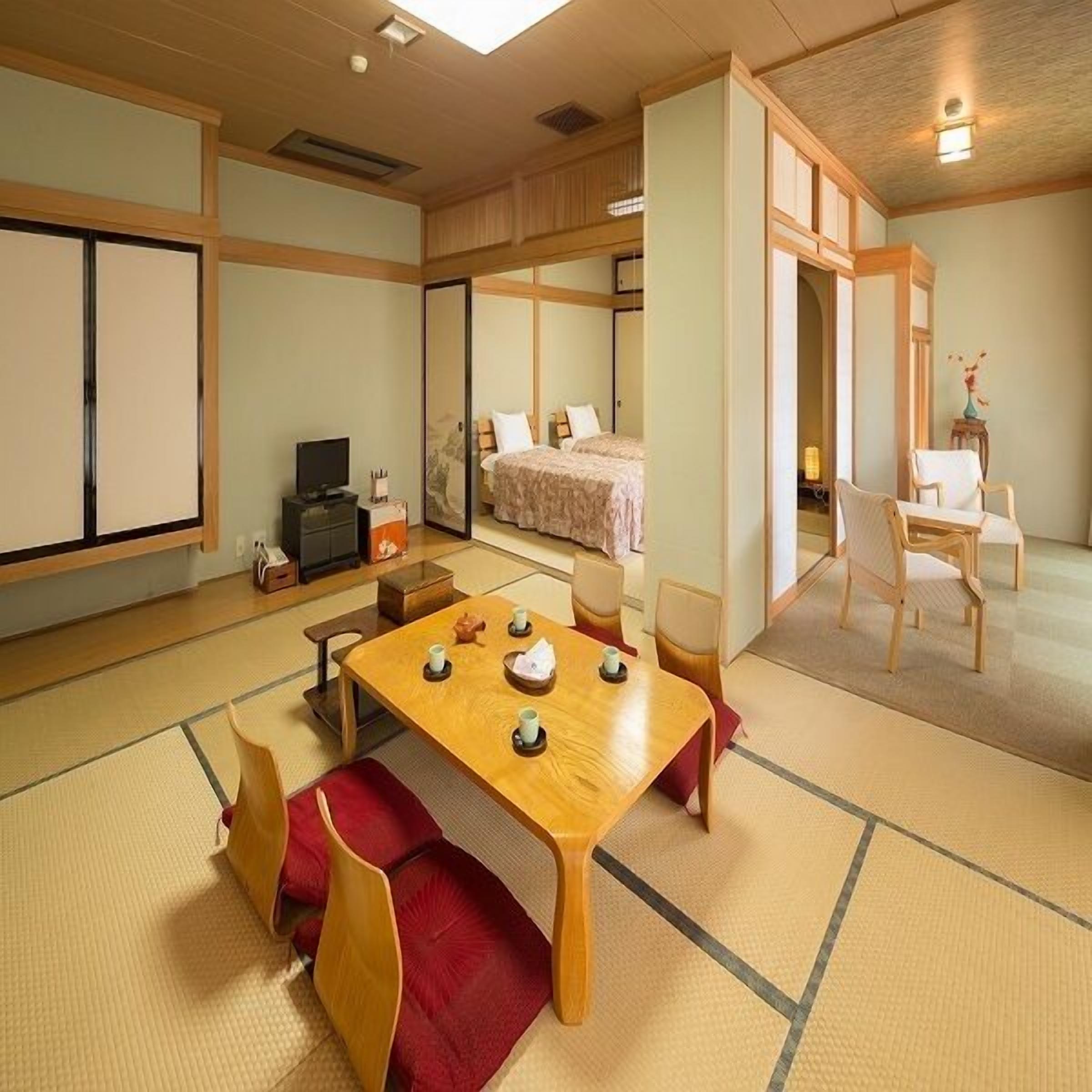 Um quarto tradicional japonês com tatames, uma mesa baixa com conjuntos de chá, uma cama com futon e portas de correr.