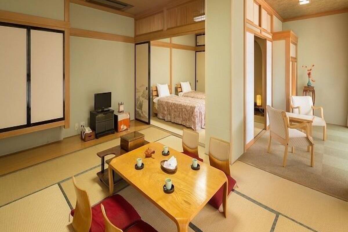 Ein traditioneller japanischer Raum mit Tatami-Böden, einem niedrigen Tisch mit Teesets, einem Bett mit Futon und Schiebetüren.