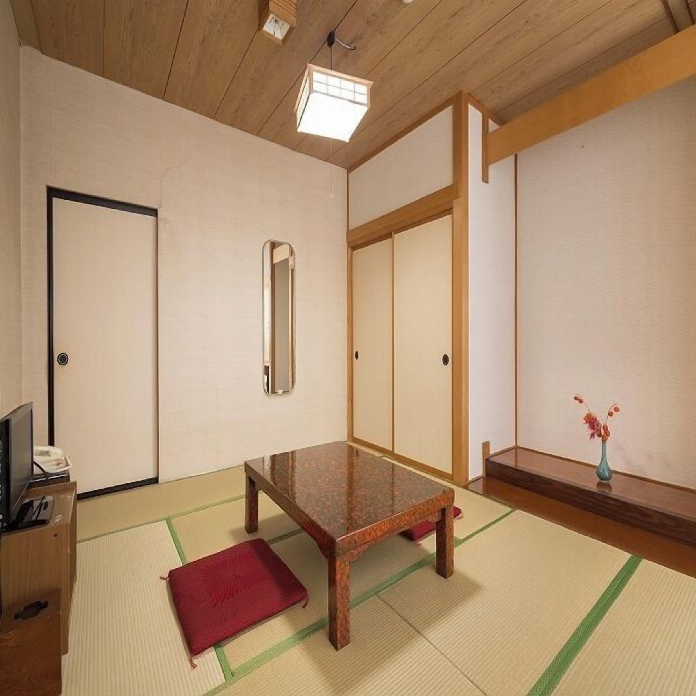 Um quarto japonês tradicional com tatames, uma mesa de madeira baixa, um espelho e uma porta deslizante.