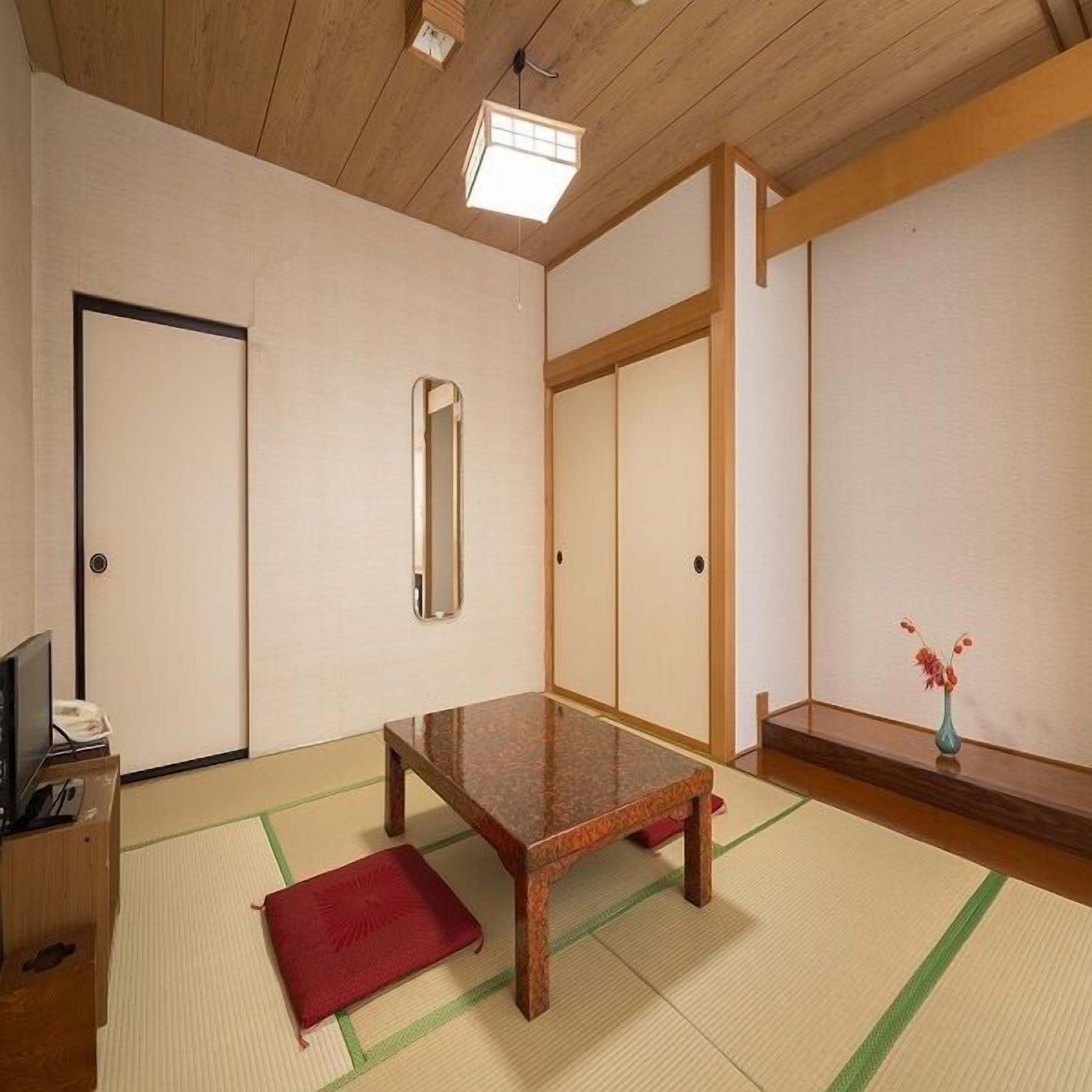 Um quarto japonês tradicional com tatames, uma mesa de madeira baixa, um espelho e portas deslizantes.