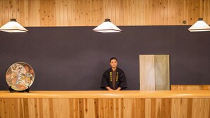 A reception desk with a person in traditional attire, a decorative plate, and three pendant lights against a wooden wall. - Nakanosawa Onsen Bandai Nishimuraya (Inawashiro)