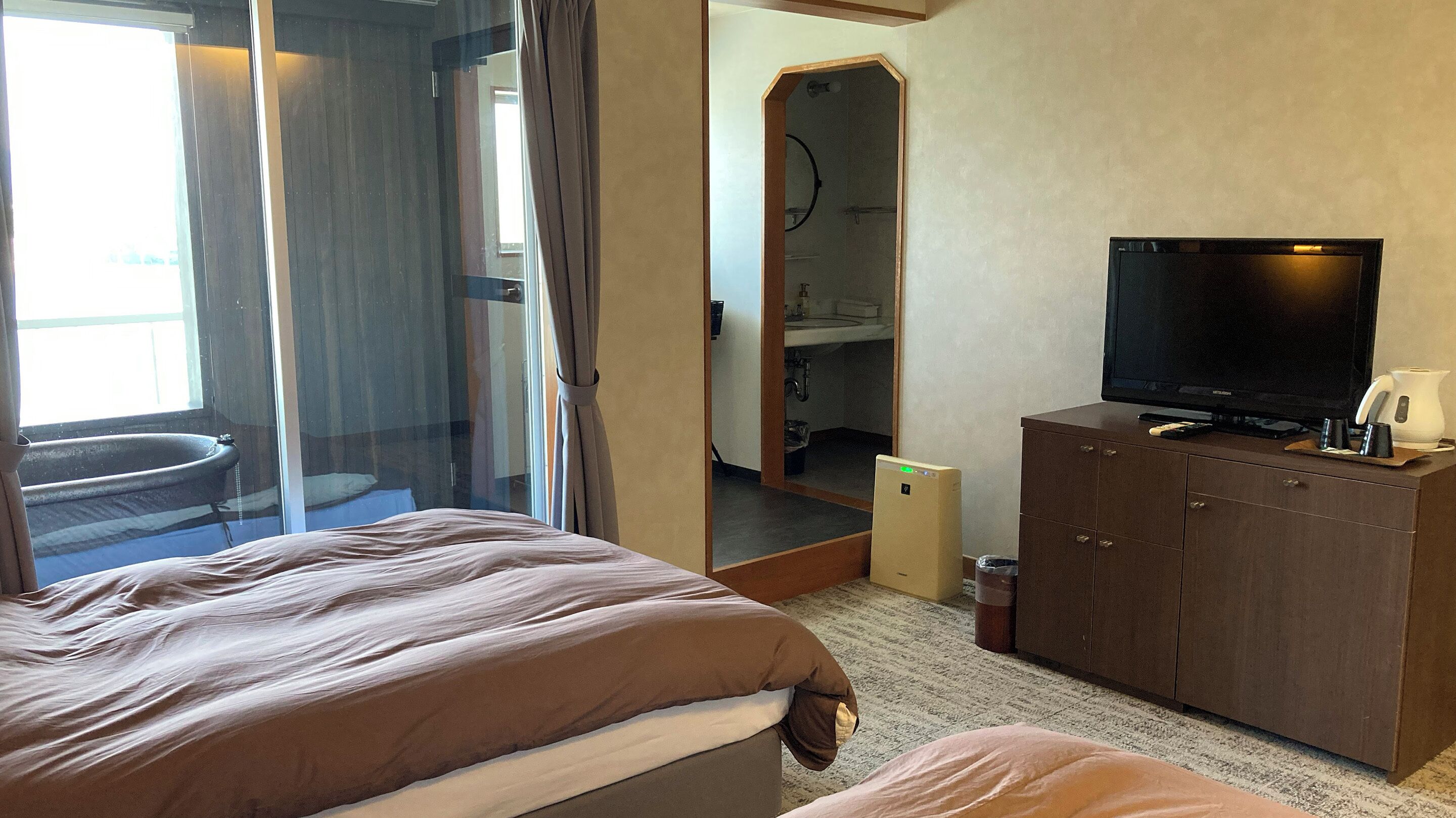A hotel room with a bed, a television, a cabinet, and a bathroom visible through a glass door.