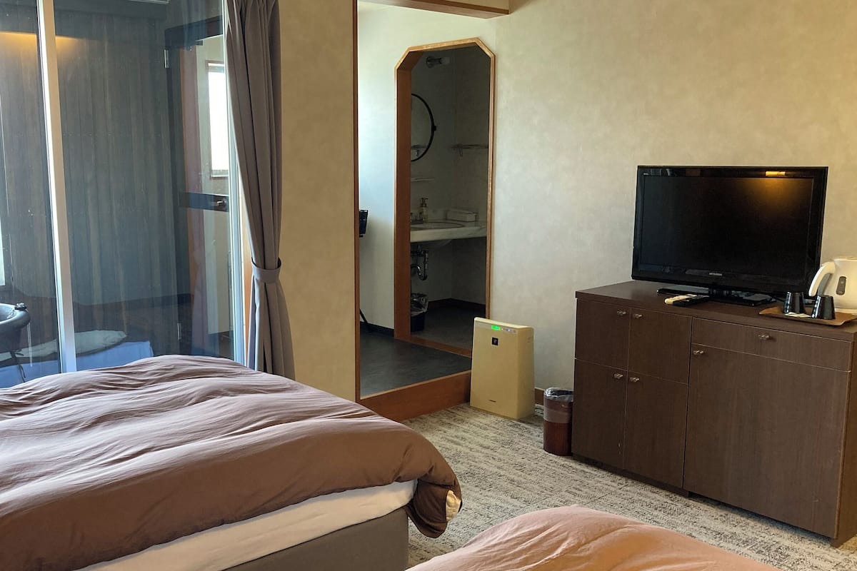 A hotel room with a bed, a television, a cabinet, and a bathroom visible through a glass door.