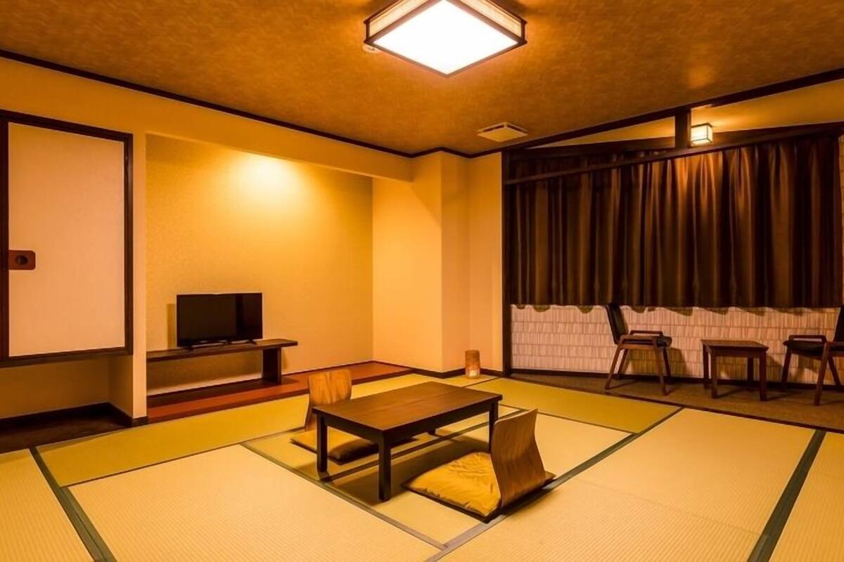 A traditional Japanese room with tatami flooring, a low table with cushions, a television, and sliding doors.