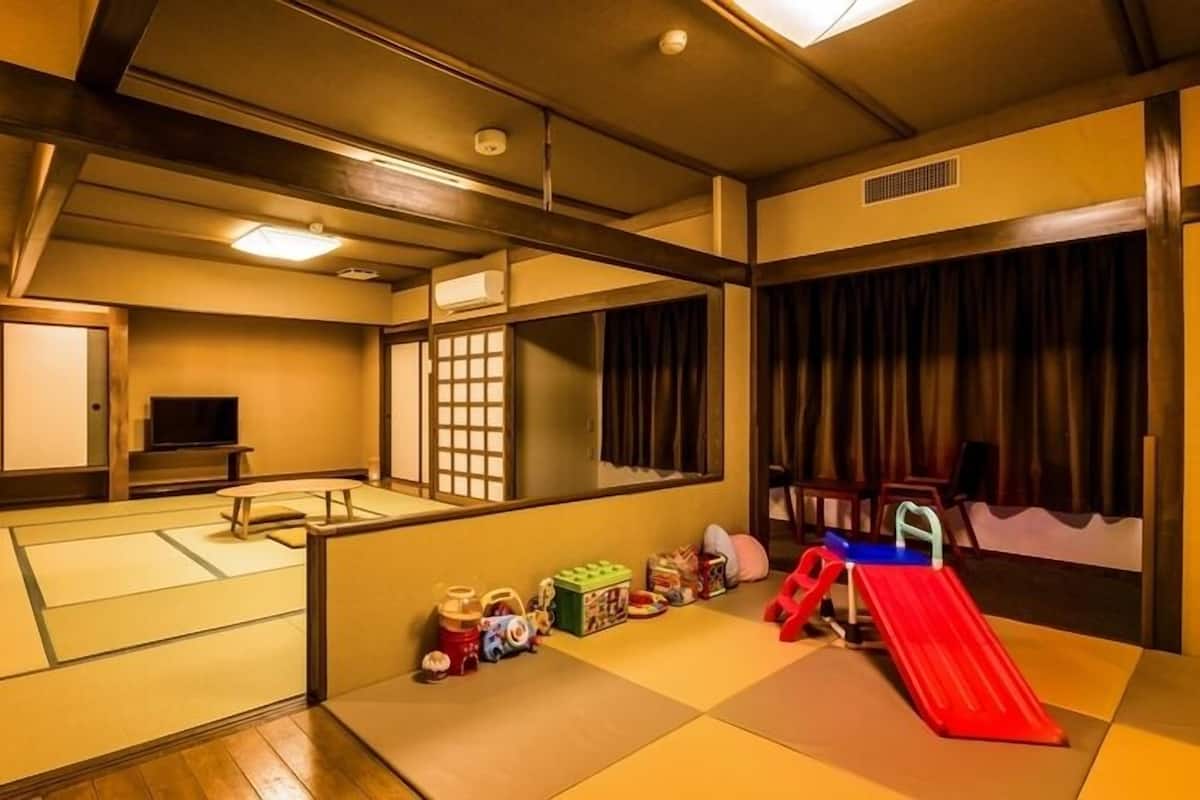 A traditional Japanese-style room with tatami flooring, a television, sliding doors, and a small play area with toys and a slide.