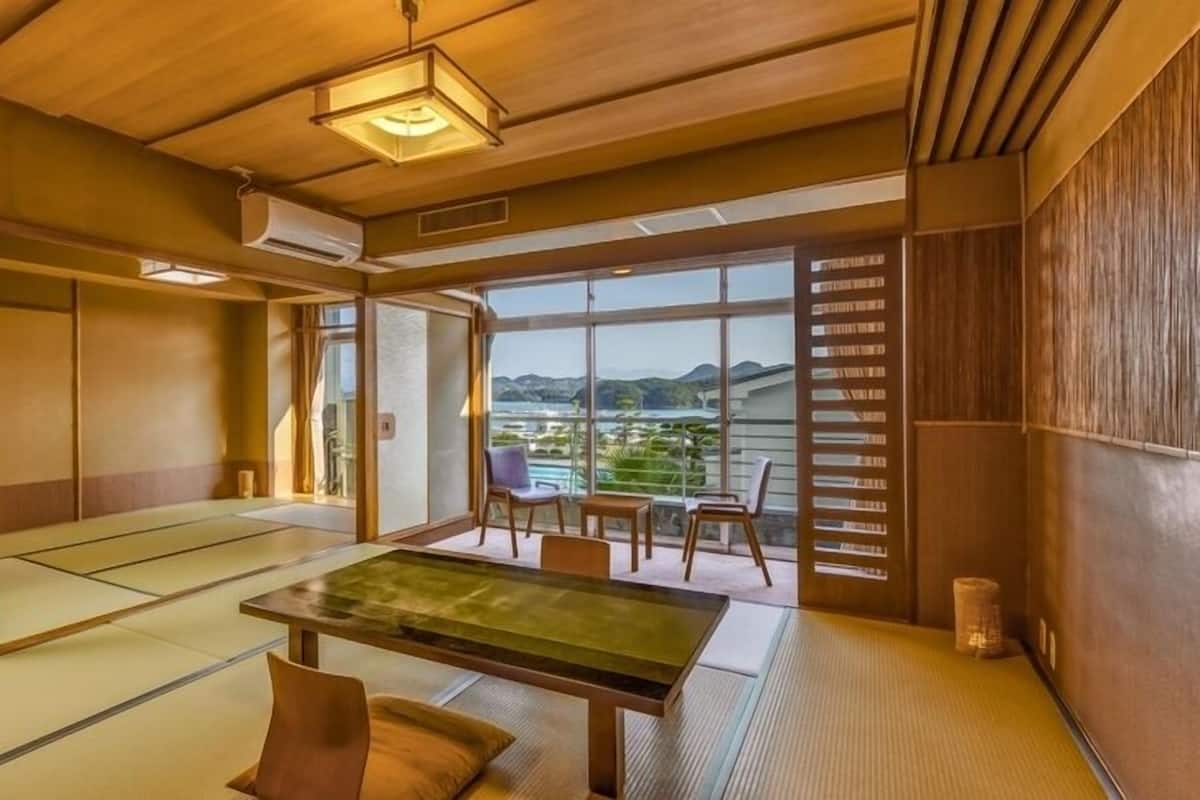 A traditional Japanese room with tatami flooring, a low table, and a view of a mountainous landscape.