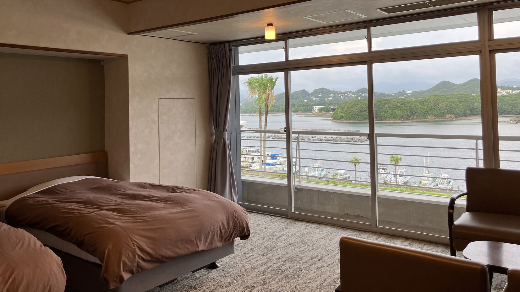 A hotel room with a bed, a chair, a view of a body of water, and a balcony.