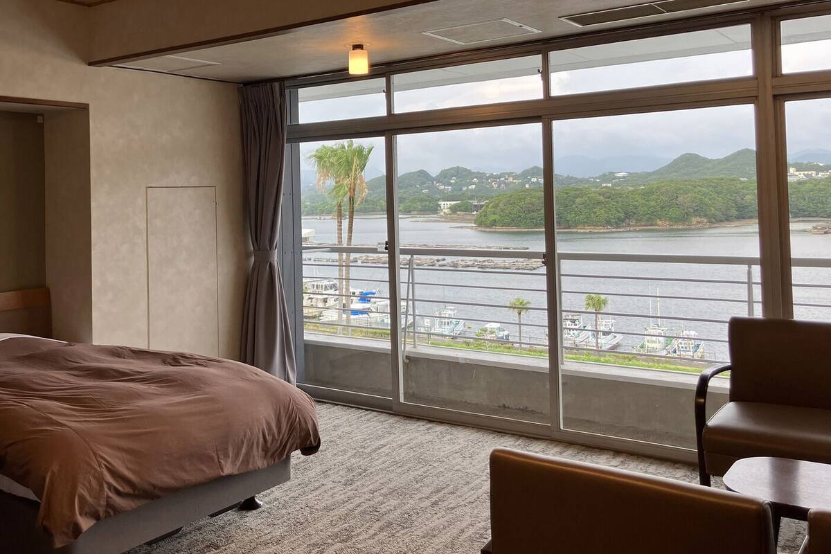 A hotel room with a bed, a chair, a view of a body of water, and a balcony.