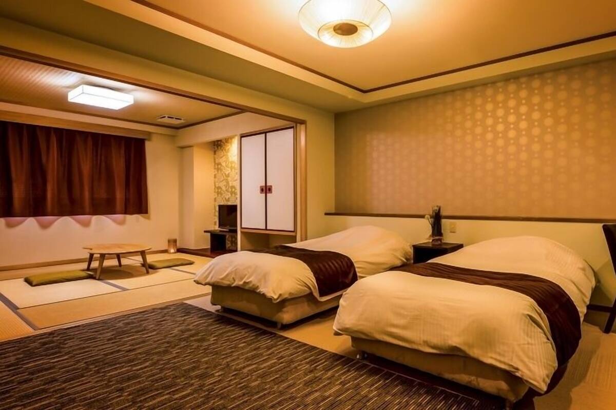 A hotel room with two beds, a sitting area, a traditional Japanese sliding door, and a patterned wall.