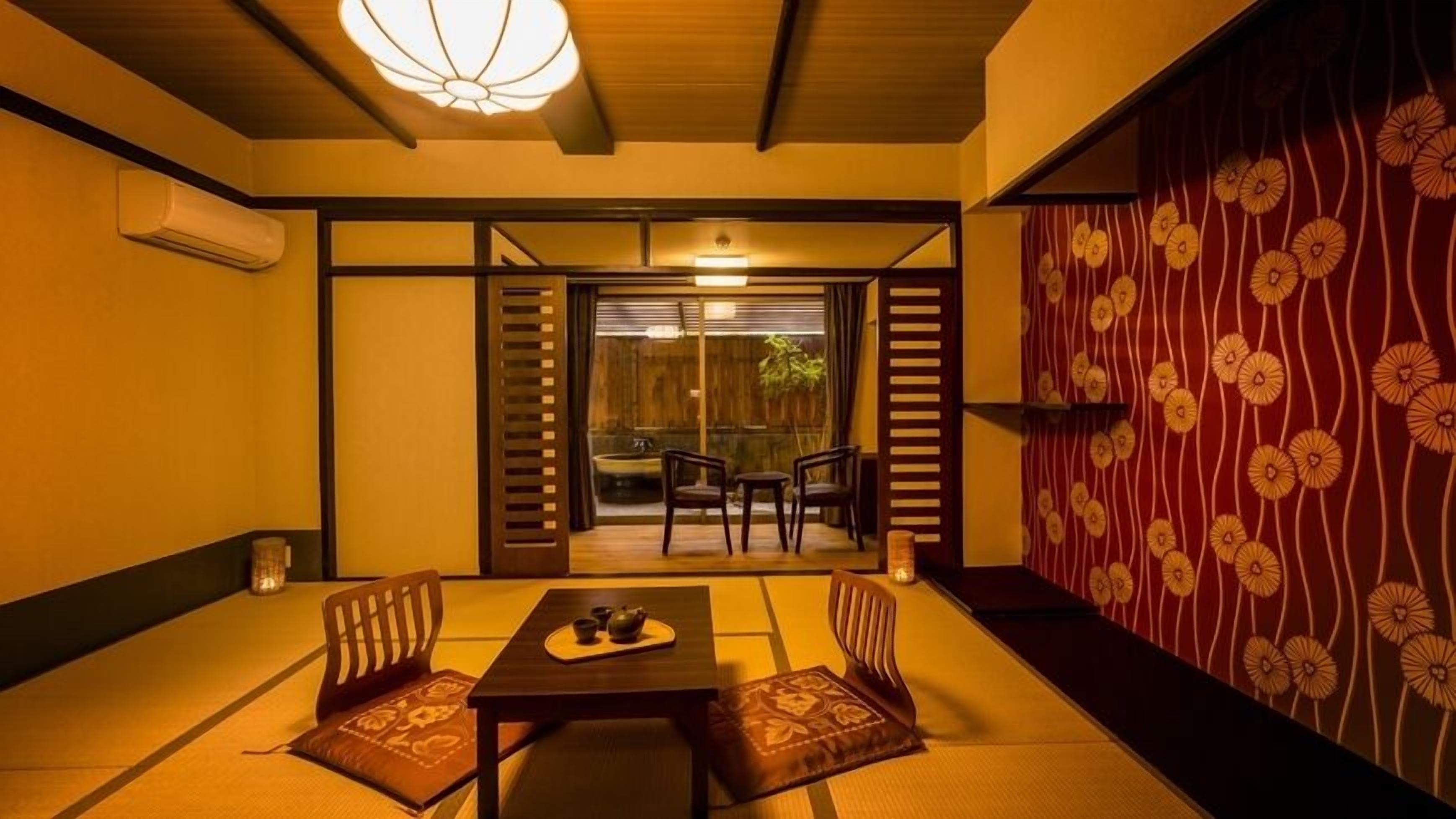 A traditional Japanese room with tatami flooring, a low table with a tea set, and sliding doors leading to an outdoor area.