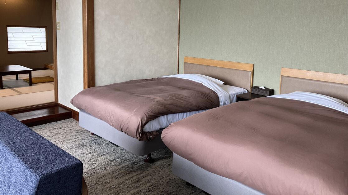 A hotel room with two beds, a small table, and a view of a traditional Japanese room.