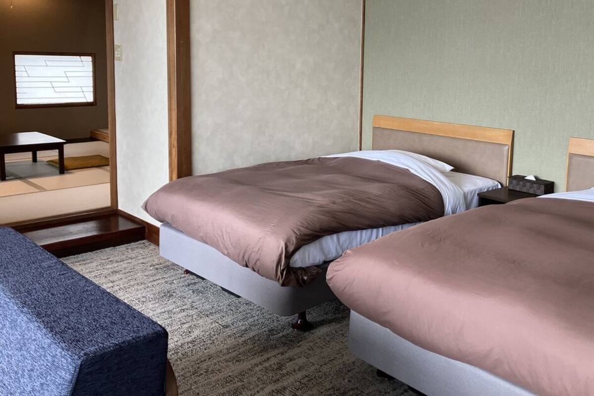 A hotel room with two beds, a small table, and a view of a traditional Japanese room.