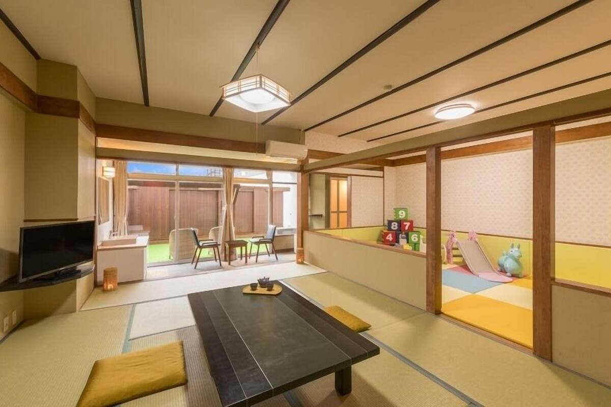 A traditional Japanese-style room with tatami flooring, a low table, a television, and a sliding door leading to an outdoor area with a playset.
