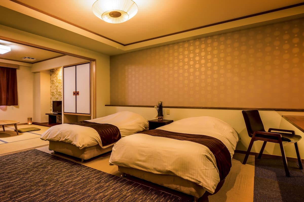 A hotel room with two beds, a sitting area, a television, and a traditional Japanese sliding door.