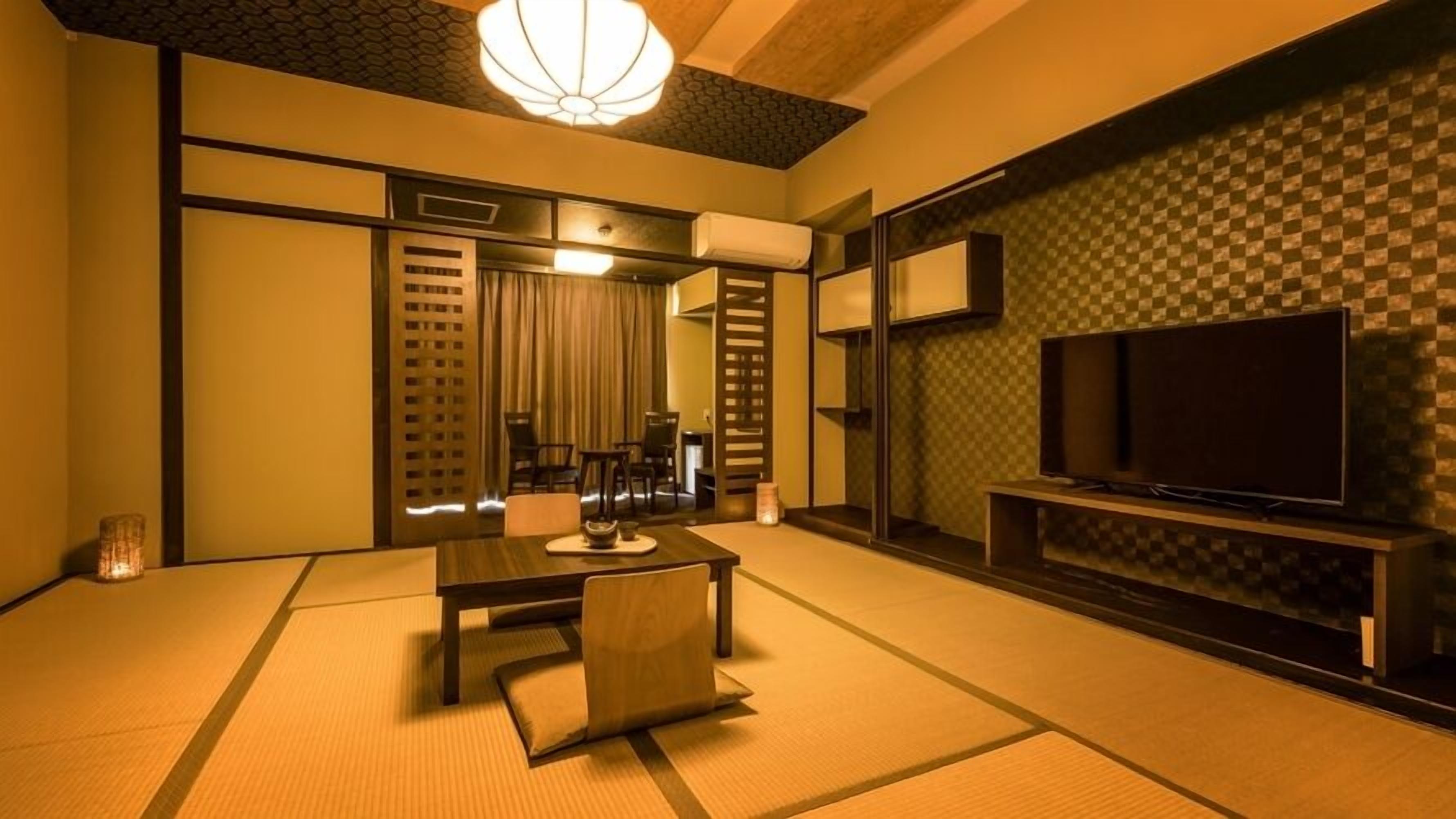 A traditional Japanese-style room with tatami flooring, a low table with cushions, a television on a stand, and a sliding door leading to another room.