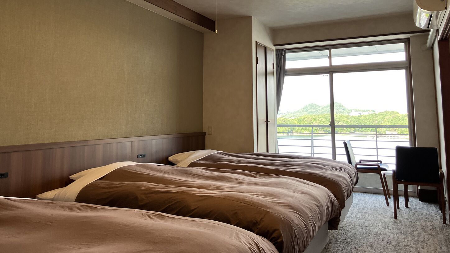 A hotel room with two beds, a chair, and a large window offering a view of greenery.