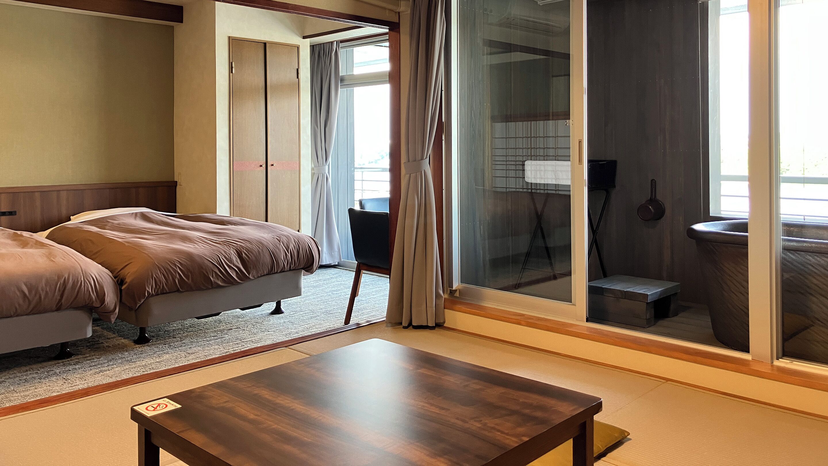 A hotel room with a bed, a small table, a chair, a sliding door, and a view of the outside.