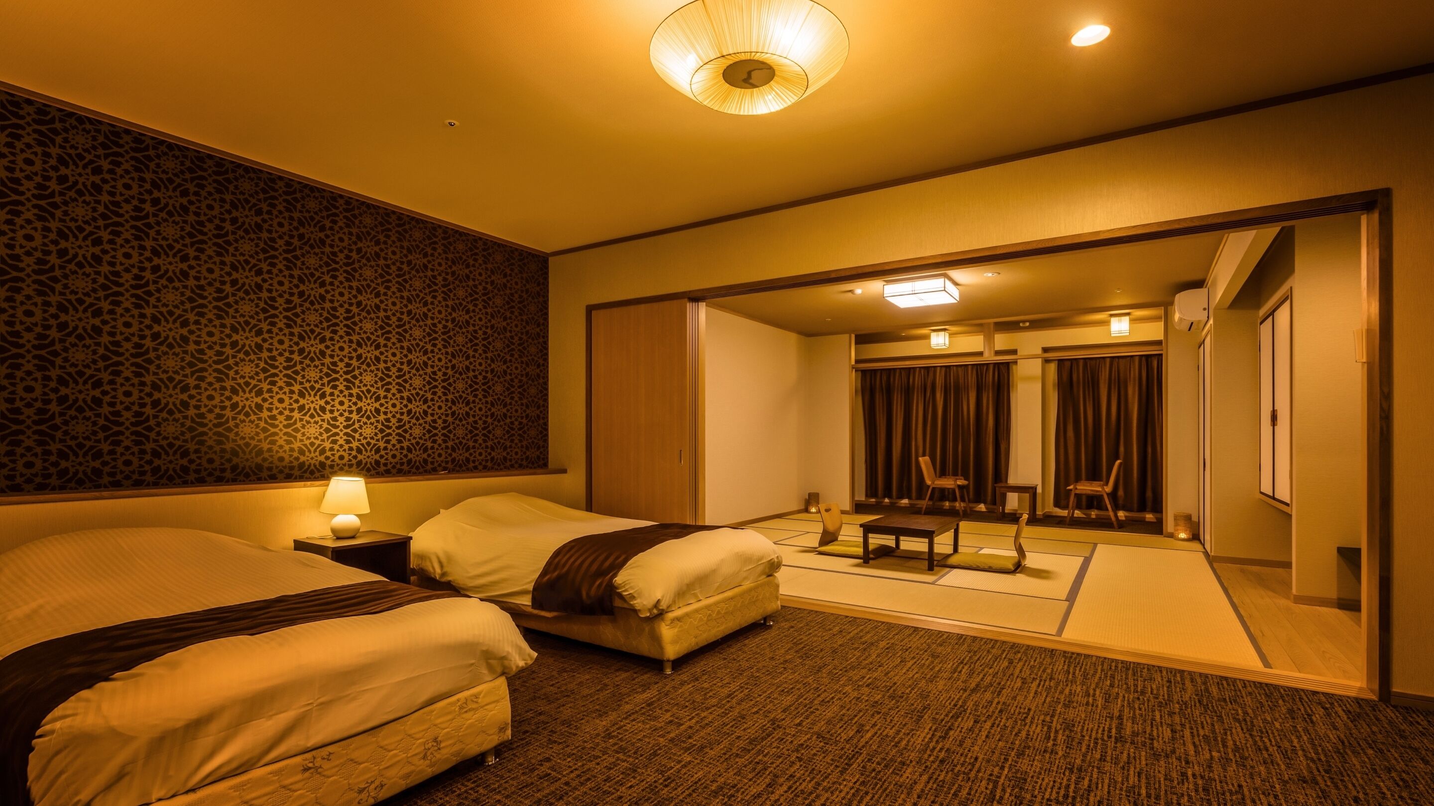 A hotel room with two beds, a sitting area with a table and chairs, and a view of a traditional Japanese room.