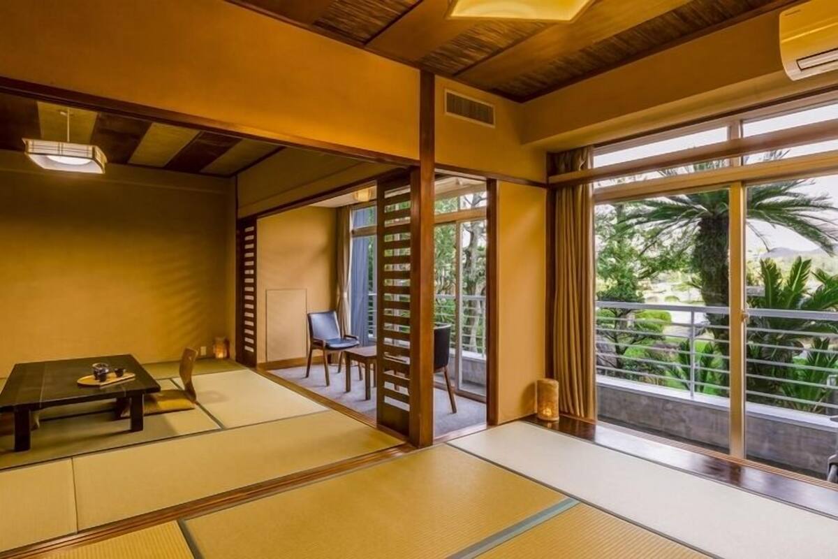 A traditional Japanese room with tatami flooring, a low table, sliding doors, and a view of greenery outside.