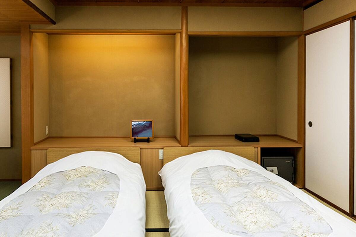 A room with two beds, a chair, a small table, and a cabinet.