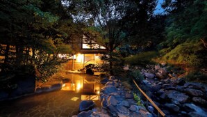 Un edificio in stile tradizionale giapponese con un vialetto lastricato che conduce a un elemento d'acqua riflettente.