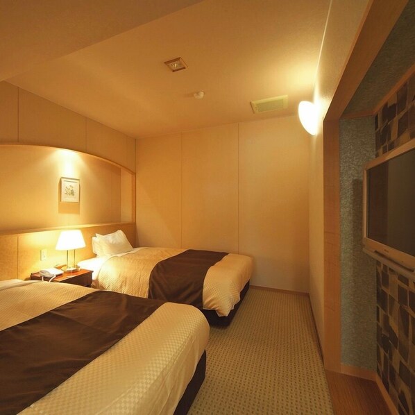 A hotel room with two beds, a nightstand with a lamp, a wall-mounted TV, and a framed picture. - Hotel Zuiyo (Atami)