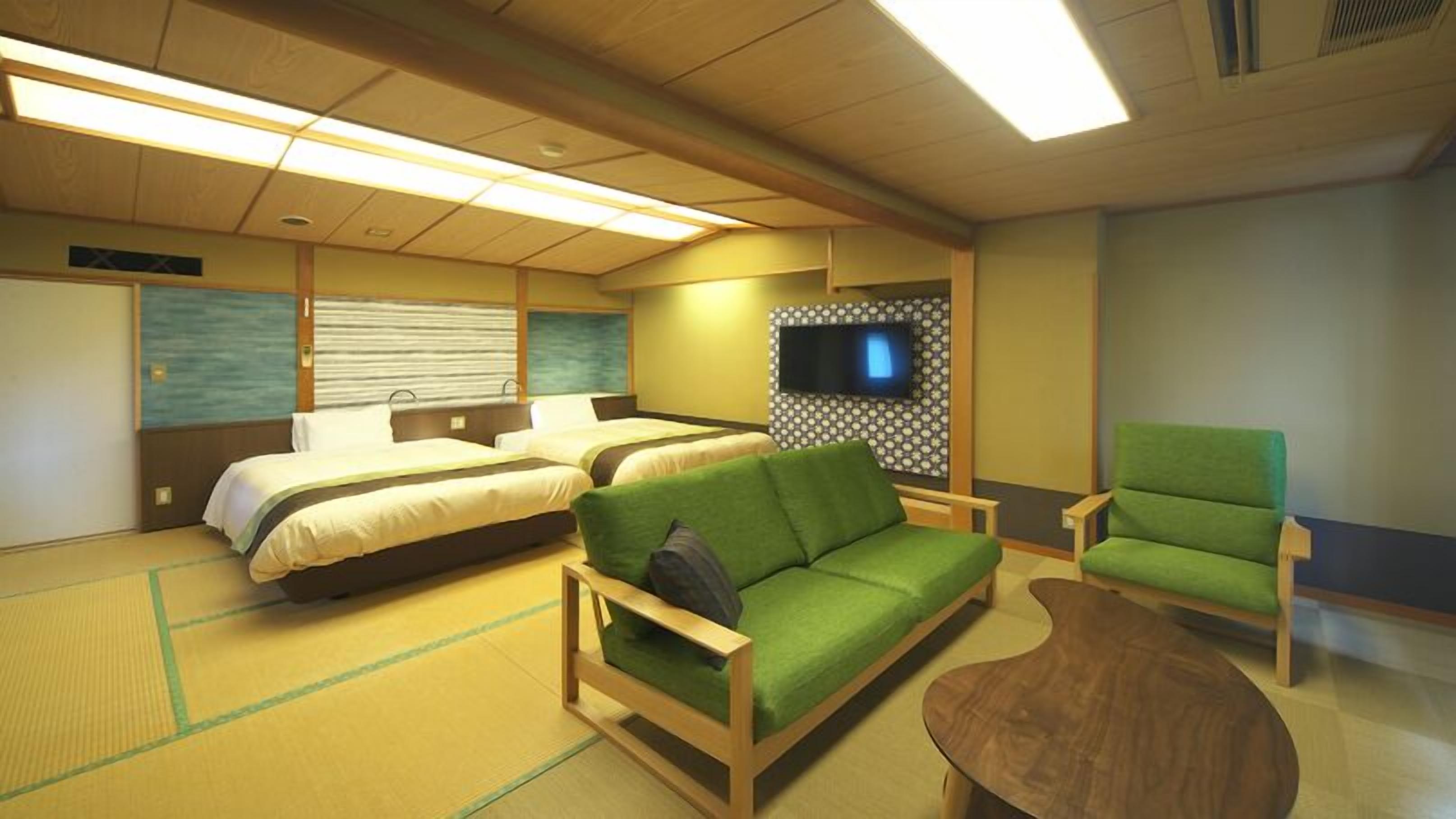 A hotel room with two beds, a green sofa, a wooden coffee table, and a TV mounted on the wall.